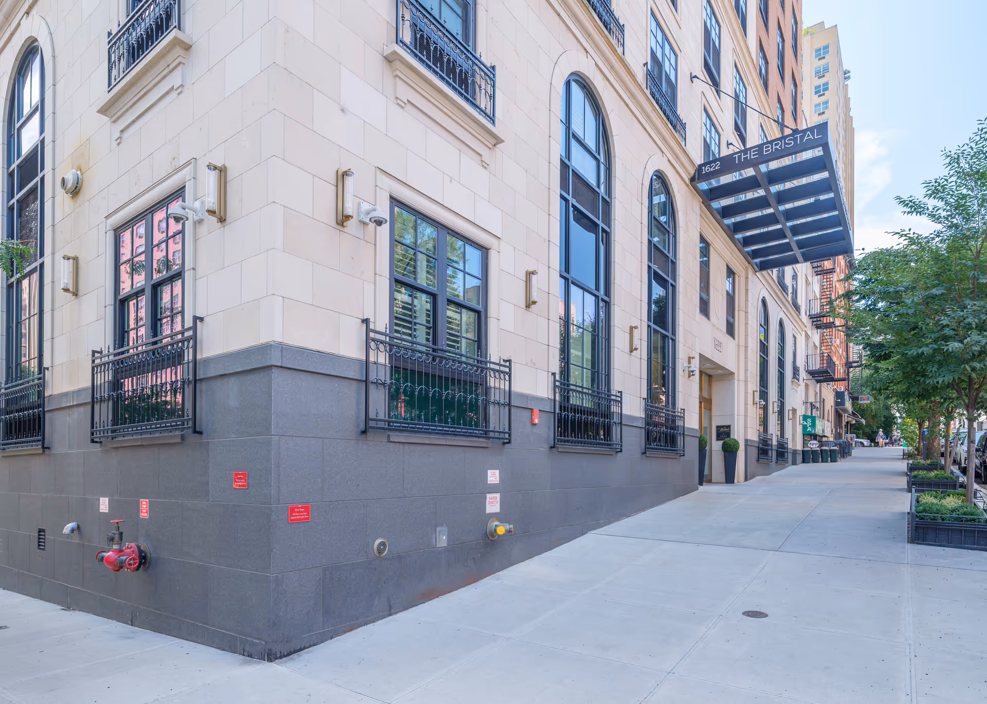 Exterior street-level view of The Bristal building facade with tall arched windows, iron railings, and a sidewalk canopy over the entrance.