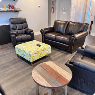 Cozy indoor lounge with black leather sofas, chairs, and a patterned ottoman.
