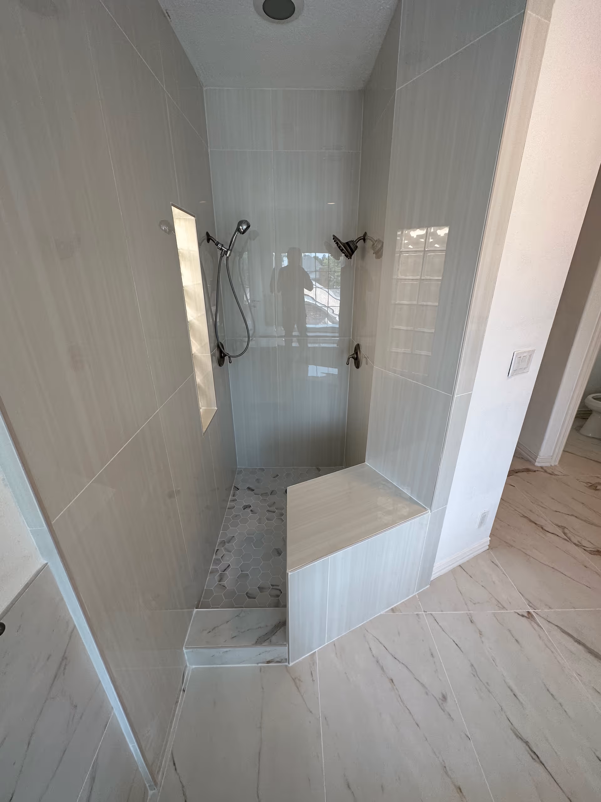 Shower area in a tiled bathroom with bench seating and dual shower heads.
