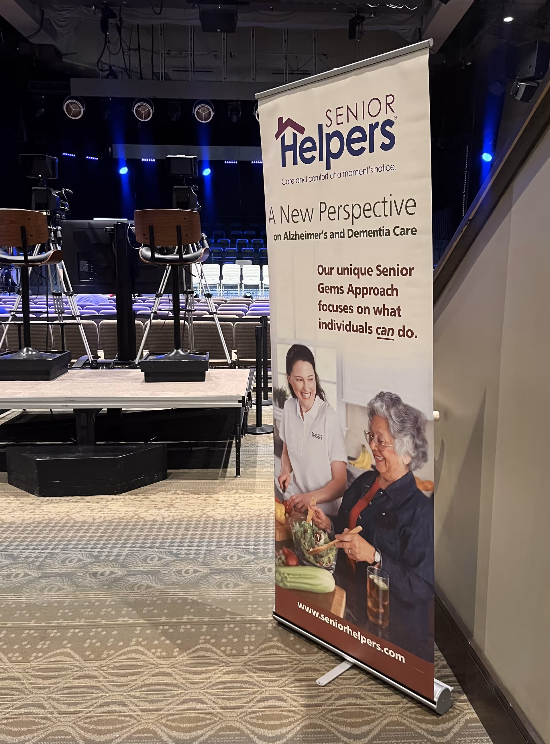 Tall Senior Helpers banner beside a stage with chairs indoors.