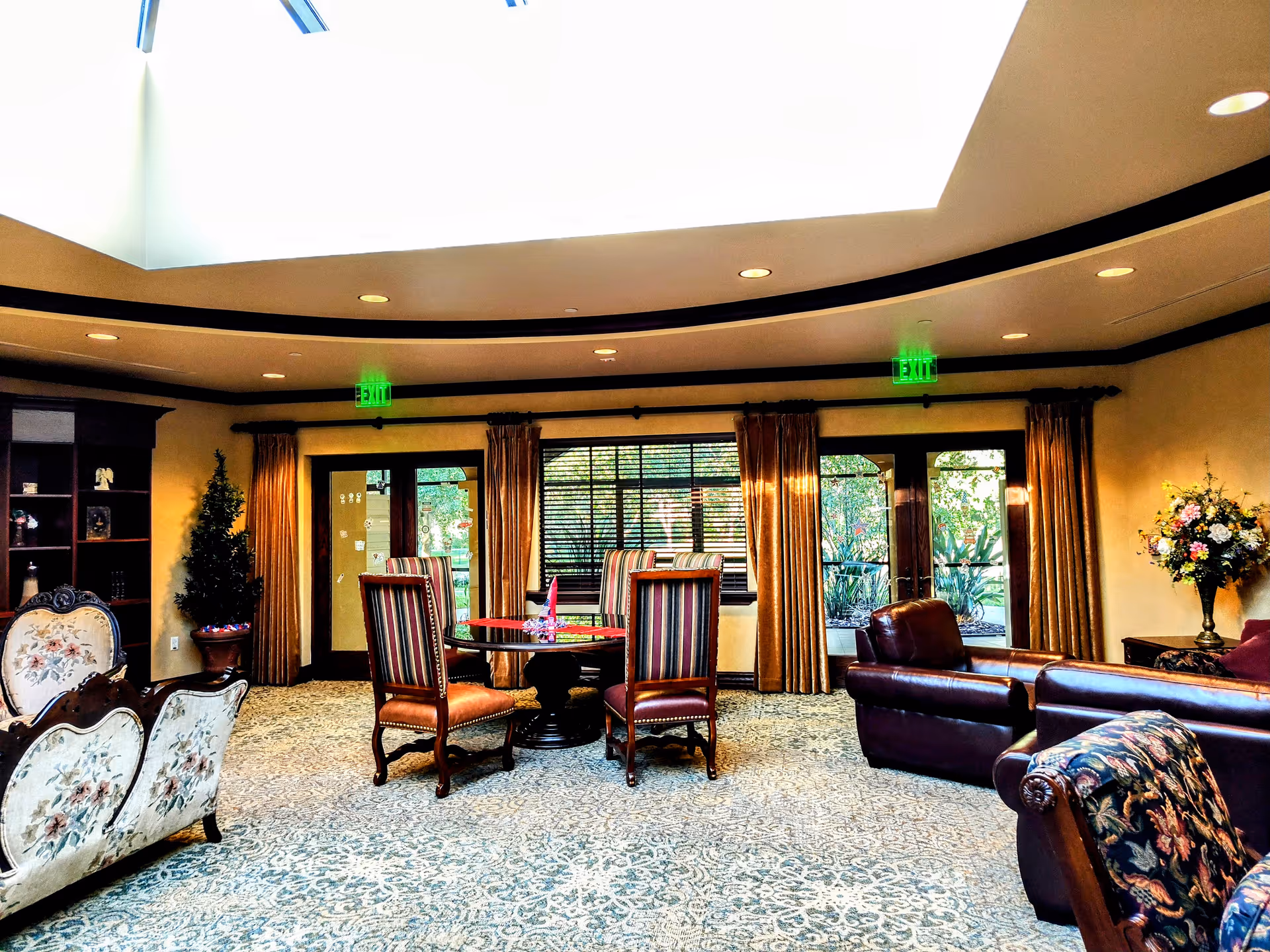 Elegant senior living lounge with round table, upholstered chairs, sofas, plants, and large windows.