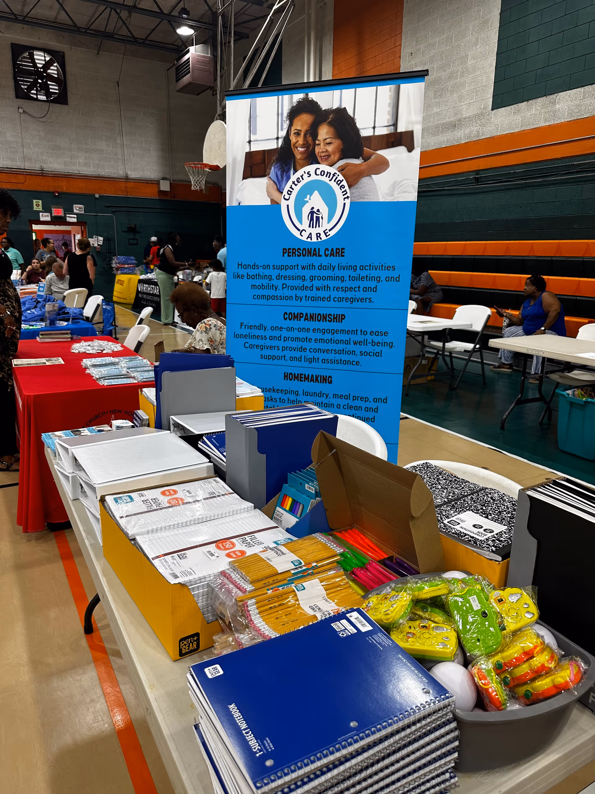 Indoor gymnasium with a Carter's Confident Care banner and tables full of supplies.