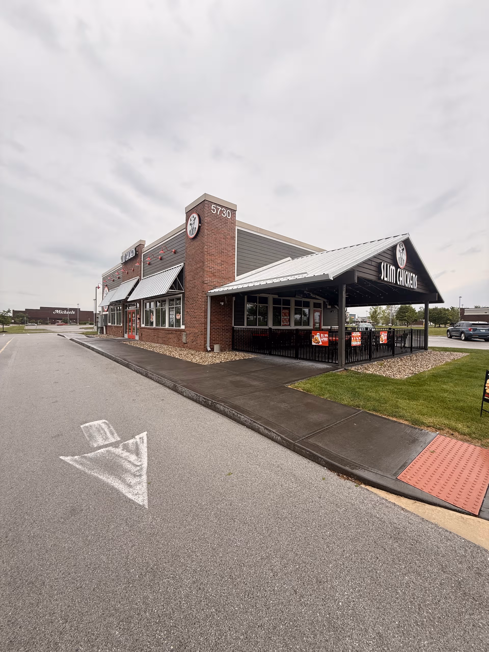 Exterior brick fast-food restaurant with Slim Chickens sign, parking lot, and covered outdoor seating.