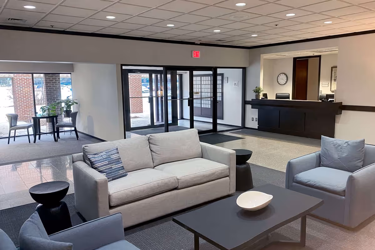 Lobby area with gray sofas, chairs, coffee table, glass doors, and a reception desk.
