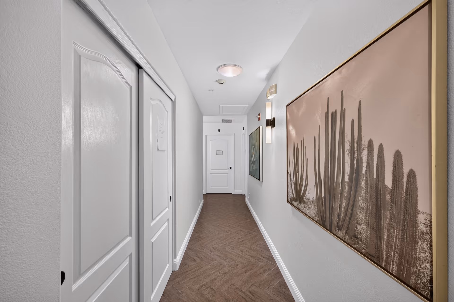 Narrow hallway in a senior living facility with closed doors and desert-themed wall art.