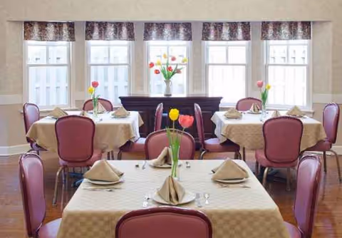 A bright senior living dining room with beige tablecloths, pink chairs, and tulip centerpieces.