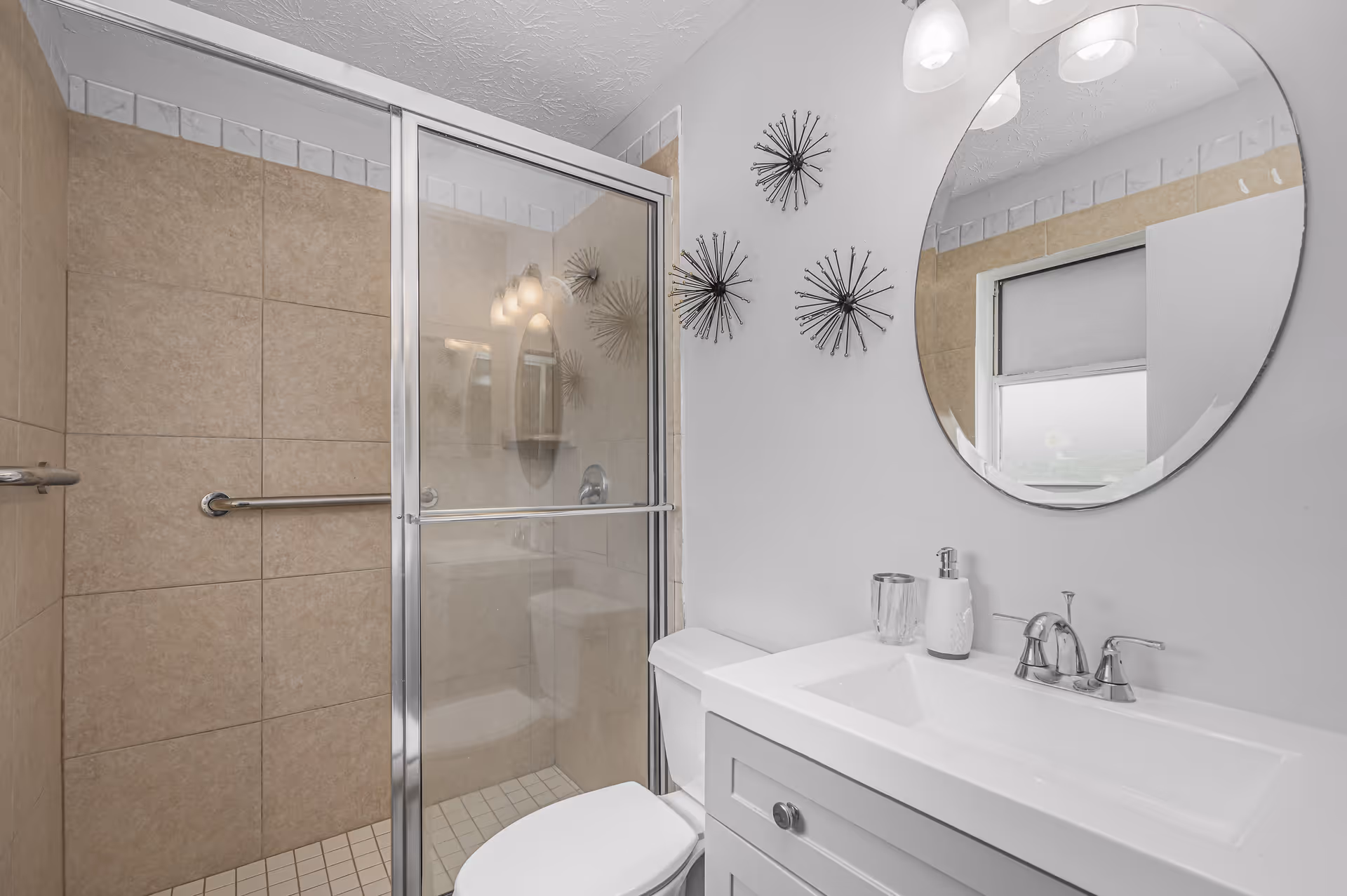 Bathroom in a senior living facility with glass shower, toilet, and oval mirror.