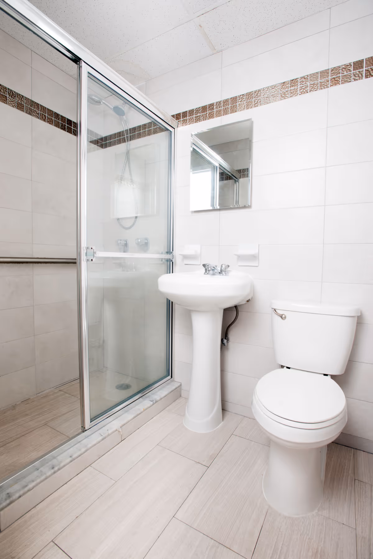 Small clean bathroom with a glass-enclosed shower, pedestal sink, and toilet.