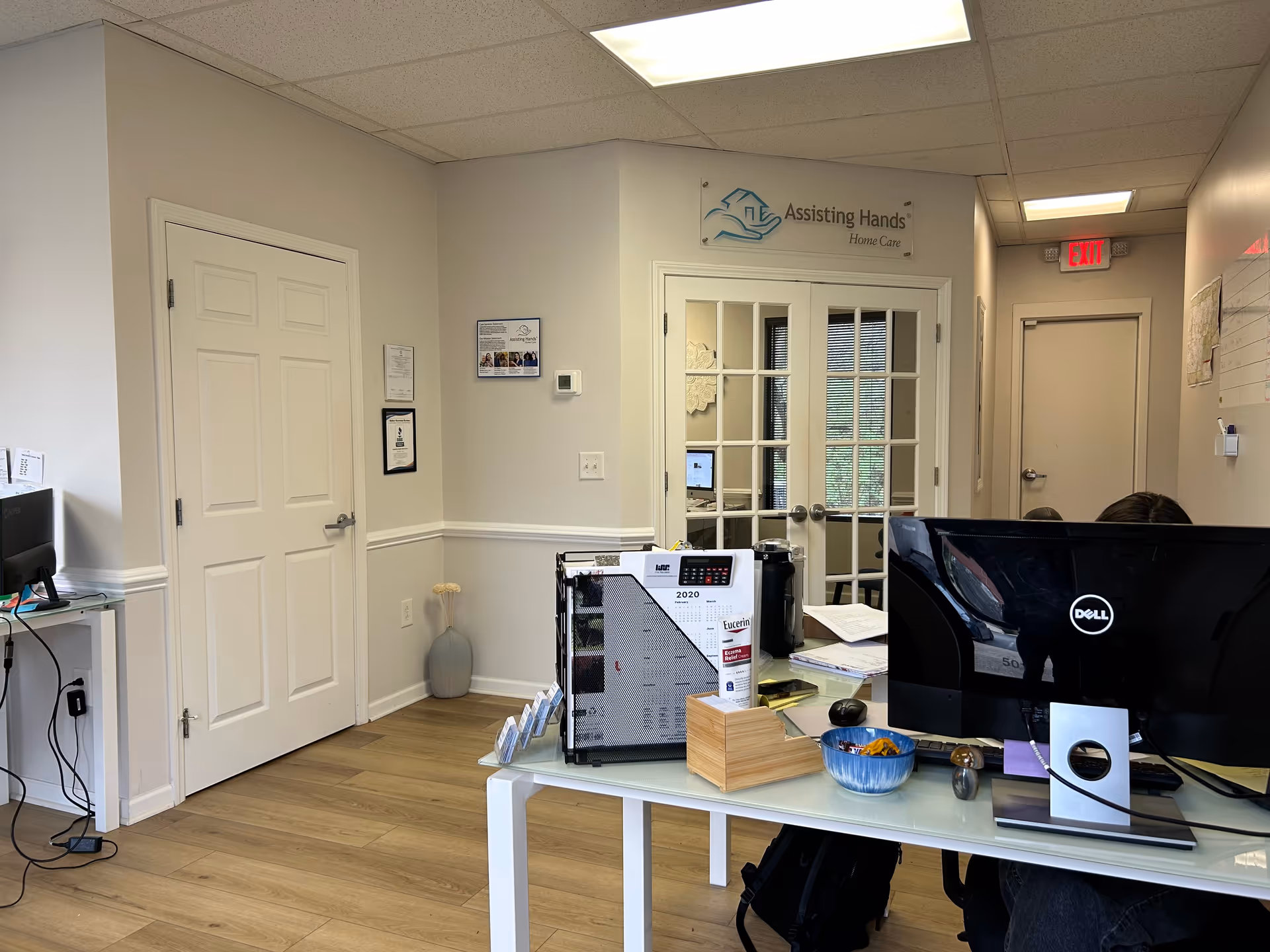 Reception desk inside a care facility, with glass-door office and Assisting Hands signage.