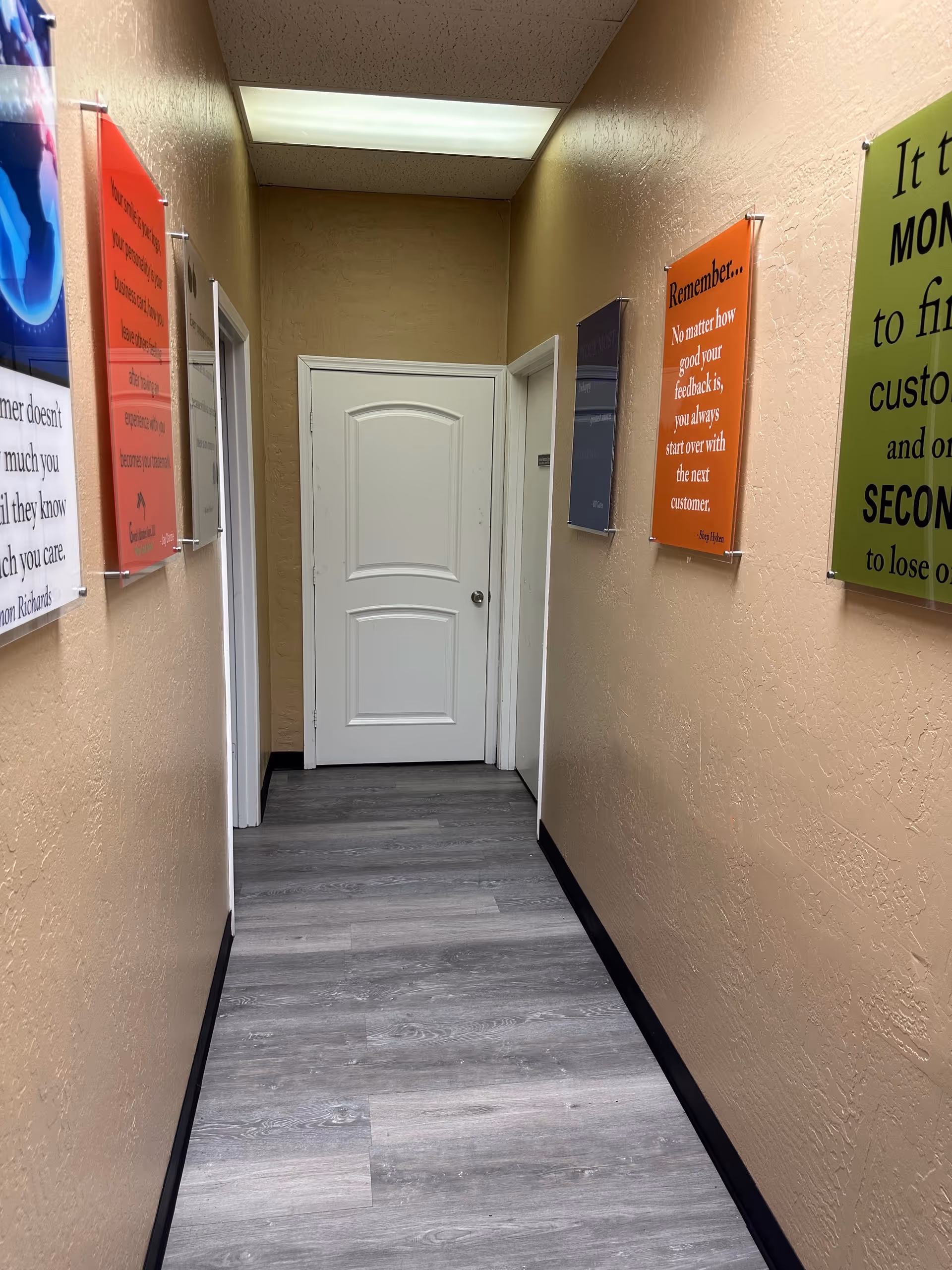 Narrow beige hallway in a care facility with posters and a white door at the end.