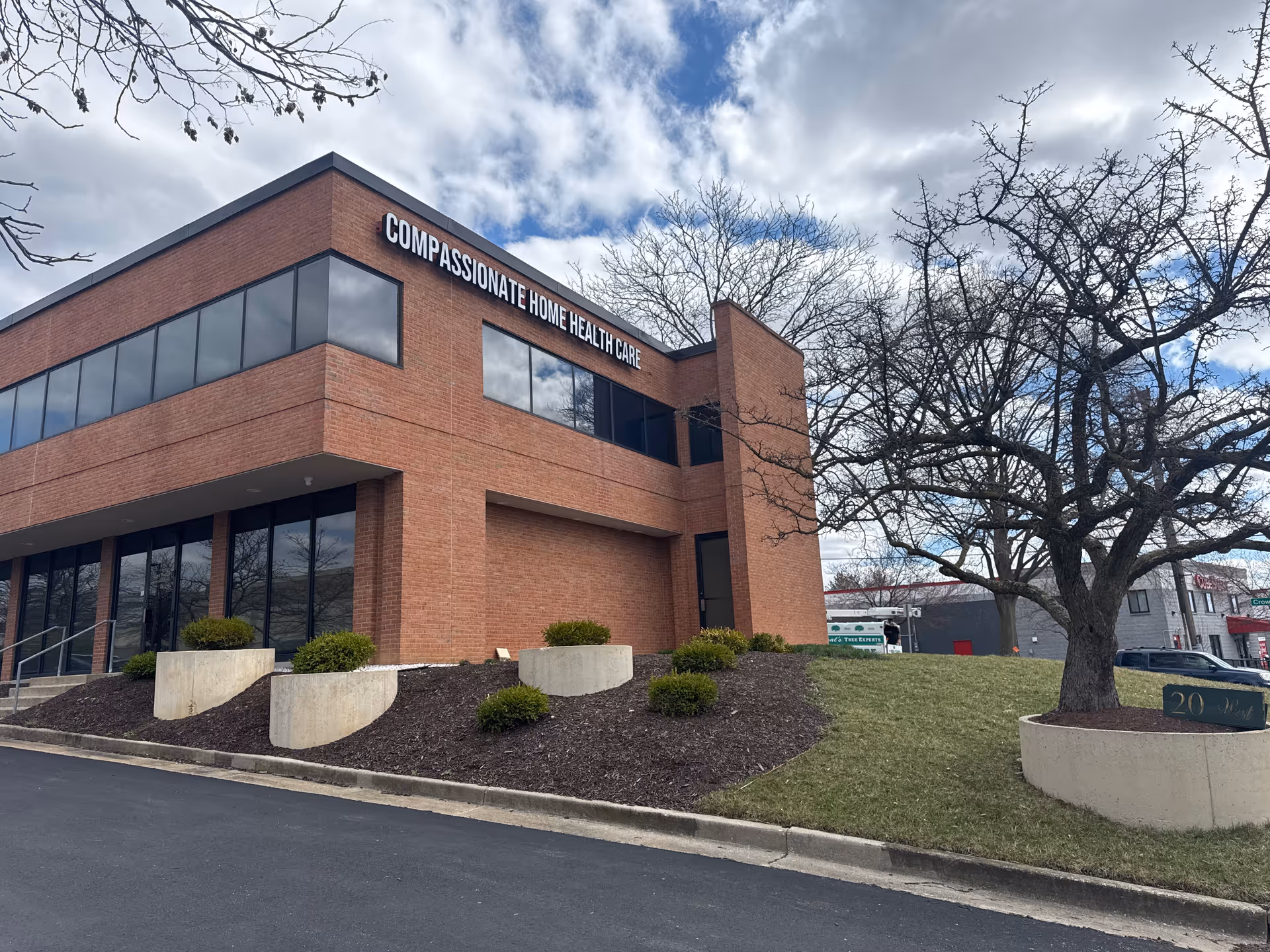 Front exterior of a brick Compassionate Home Health Care building with landscaping.