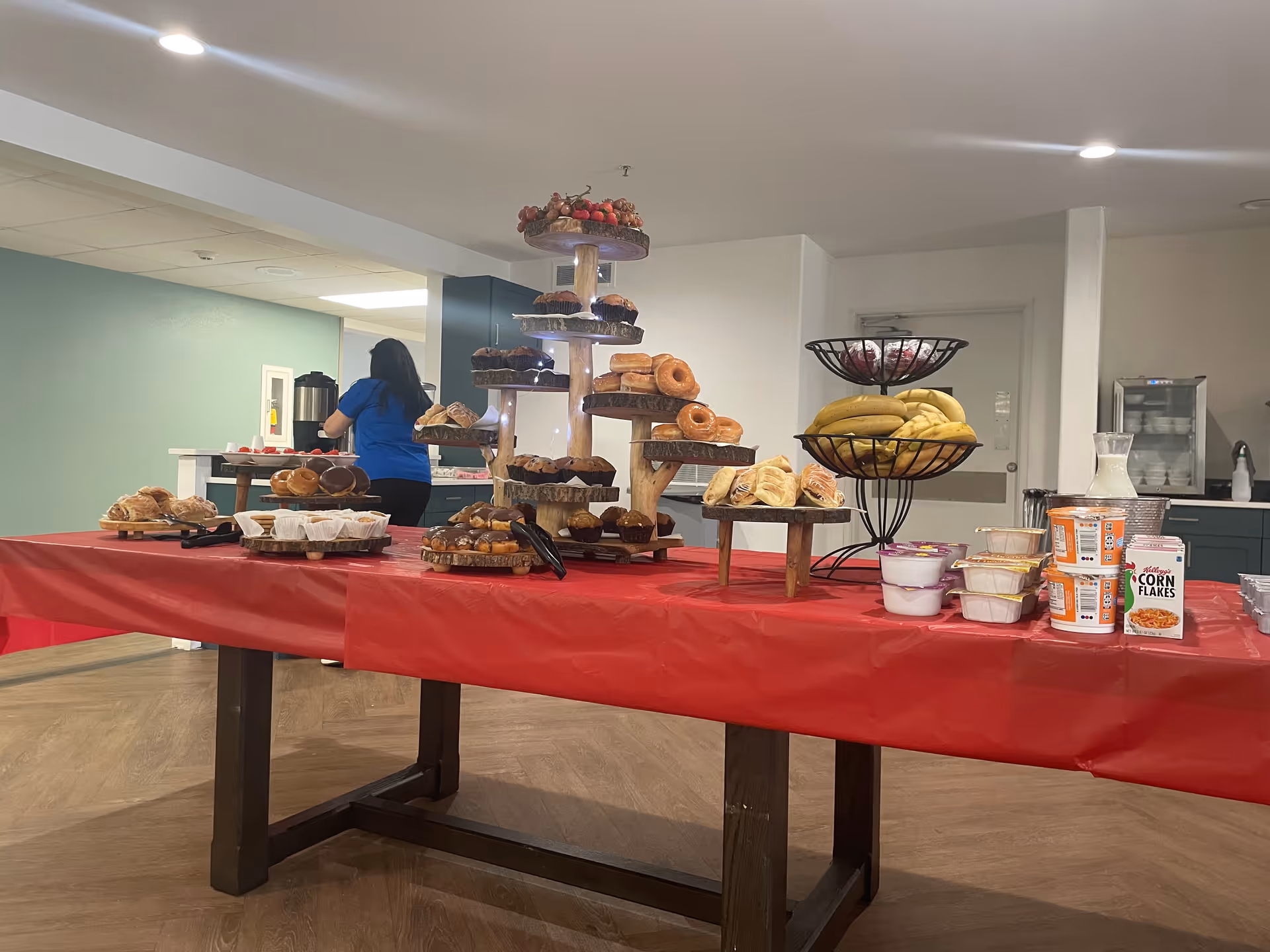 Long dining table with pastries and donuts, plus yogurt cups; staff in blue in background.