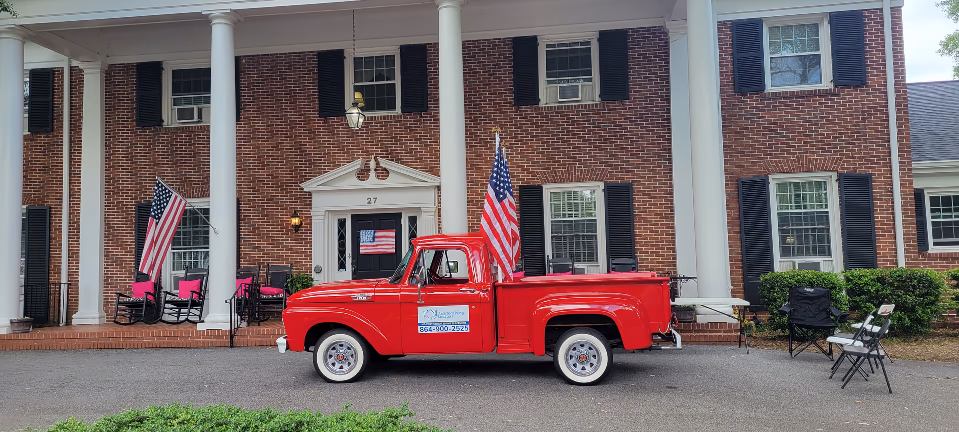 Brick building with white columns, American flags, and a red vintage pickup parked out front.