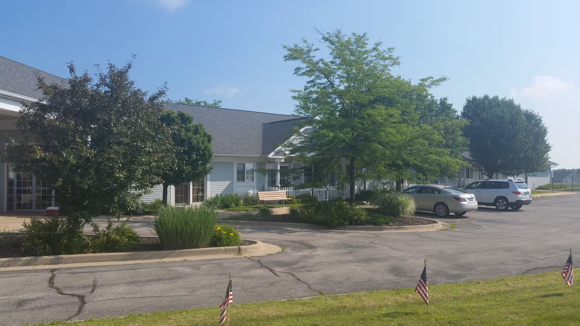 Exterior view of Dimensions Living Winnebago building with trees, benches, and parked cars.