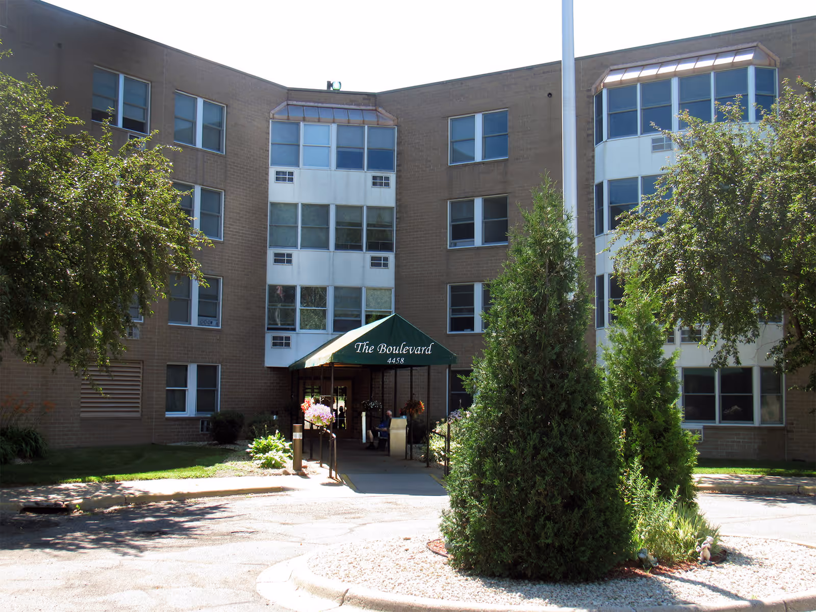 Front entrance of a multi-story brick senior living building with a green awning reading 'The Boulevard' and trees in the foreground.