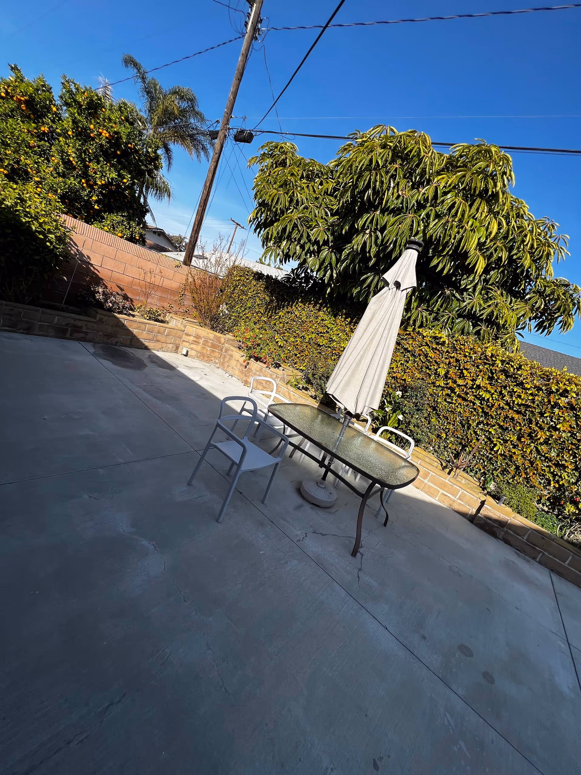 Outdoor patio with glass table, closed umbrella, and white chairs.