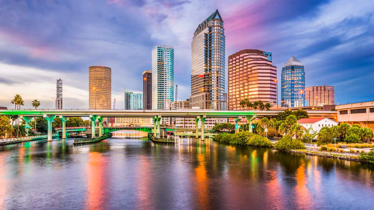 Sunset-lit city skyline over a river with bridges and tall modern buildings.