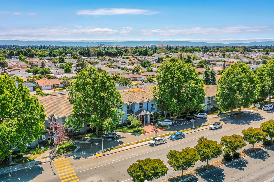 Aerial view of a senior housing campus with tree-lined streets and parked cars.