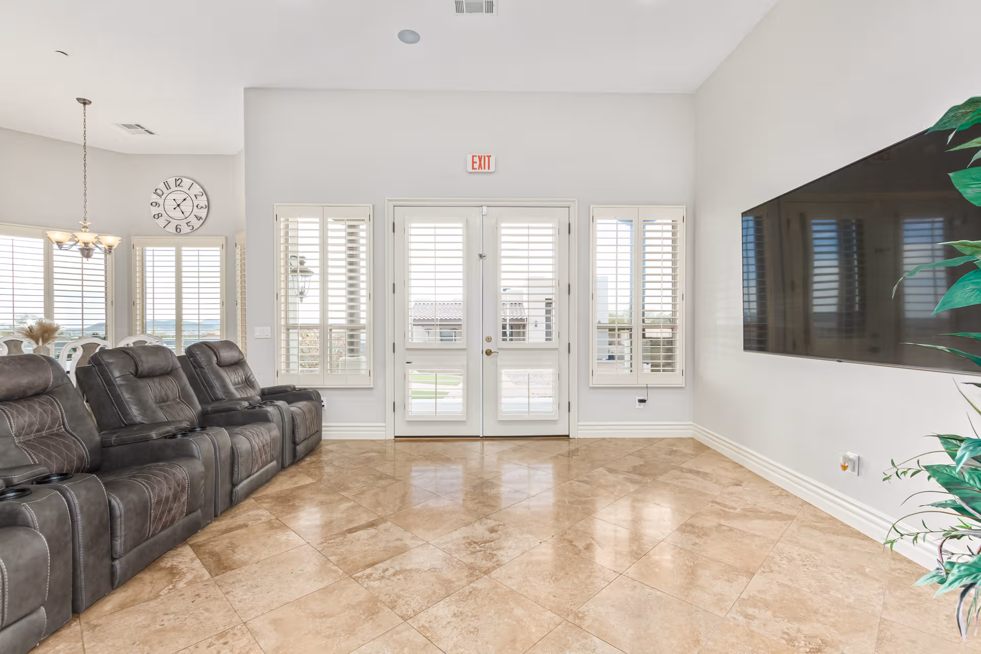Bright lobby with row of recliner chairs, TV, clock, and glass exit doors.