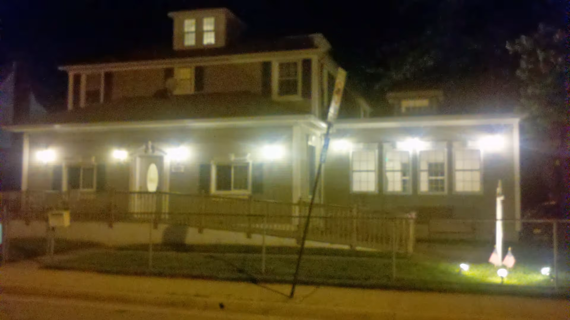 Night exterior of a two-story assisted living facility with lit porch and fence.