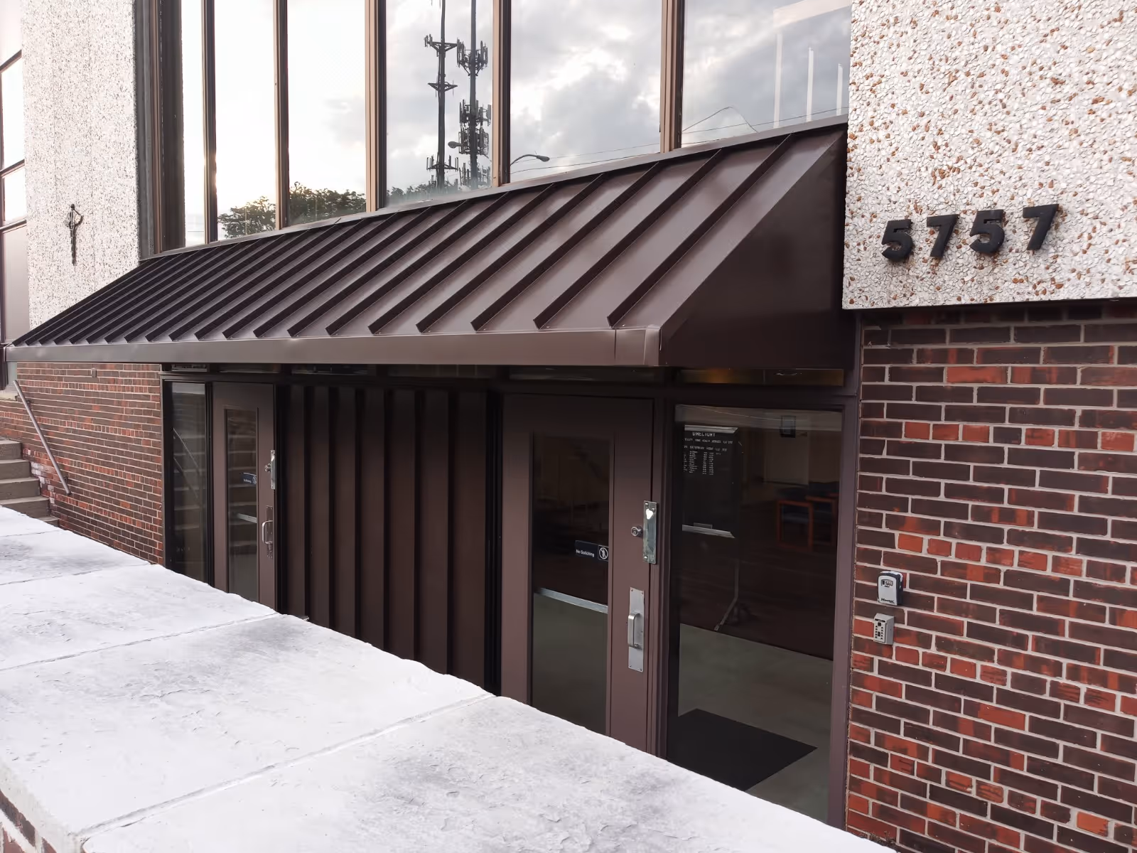 A brick building entrance with glass doors and a metal awning.