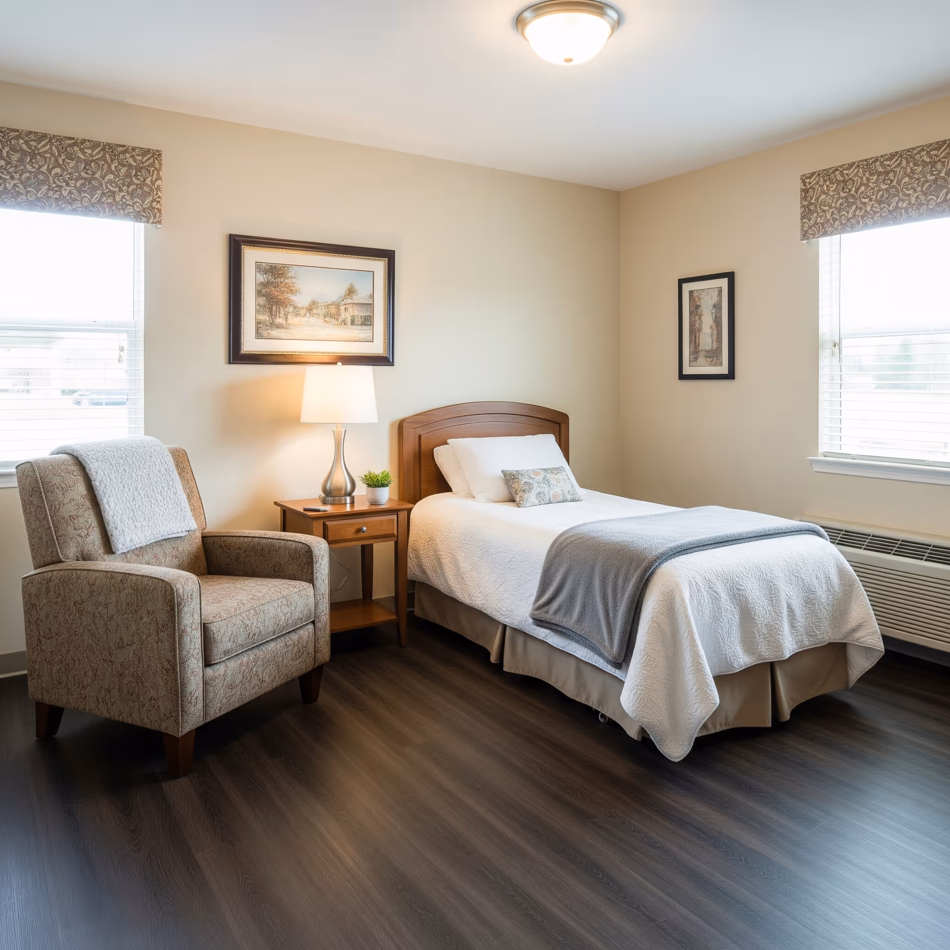 A neatly furnished single bedroom with bed, chair, lamp, and framed wall art.