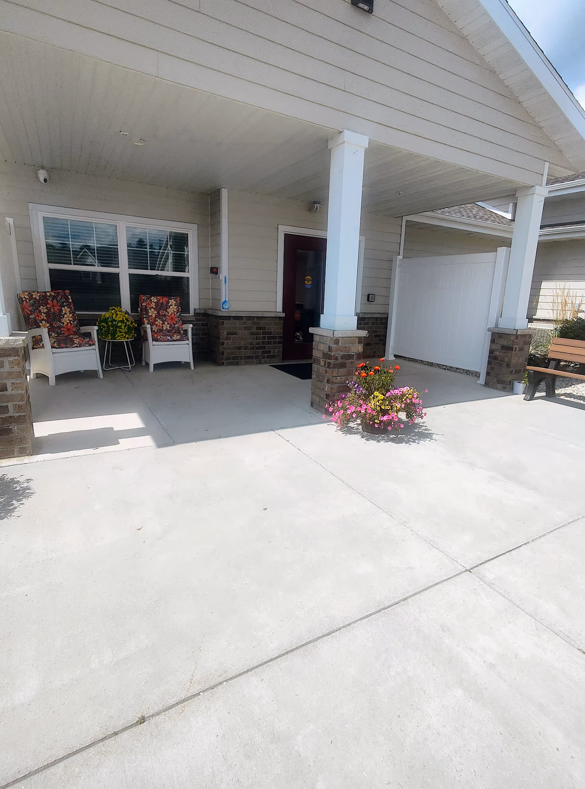 Front porch of Kettle Moraine Gardens with chairs, potted flowers, and a bench.