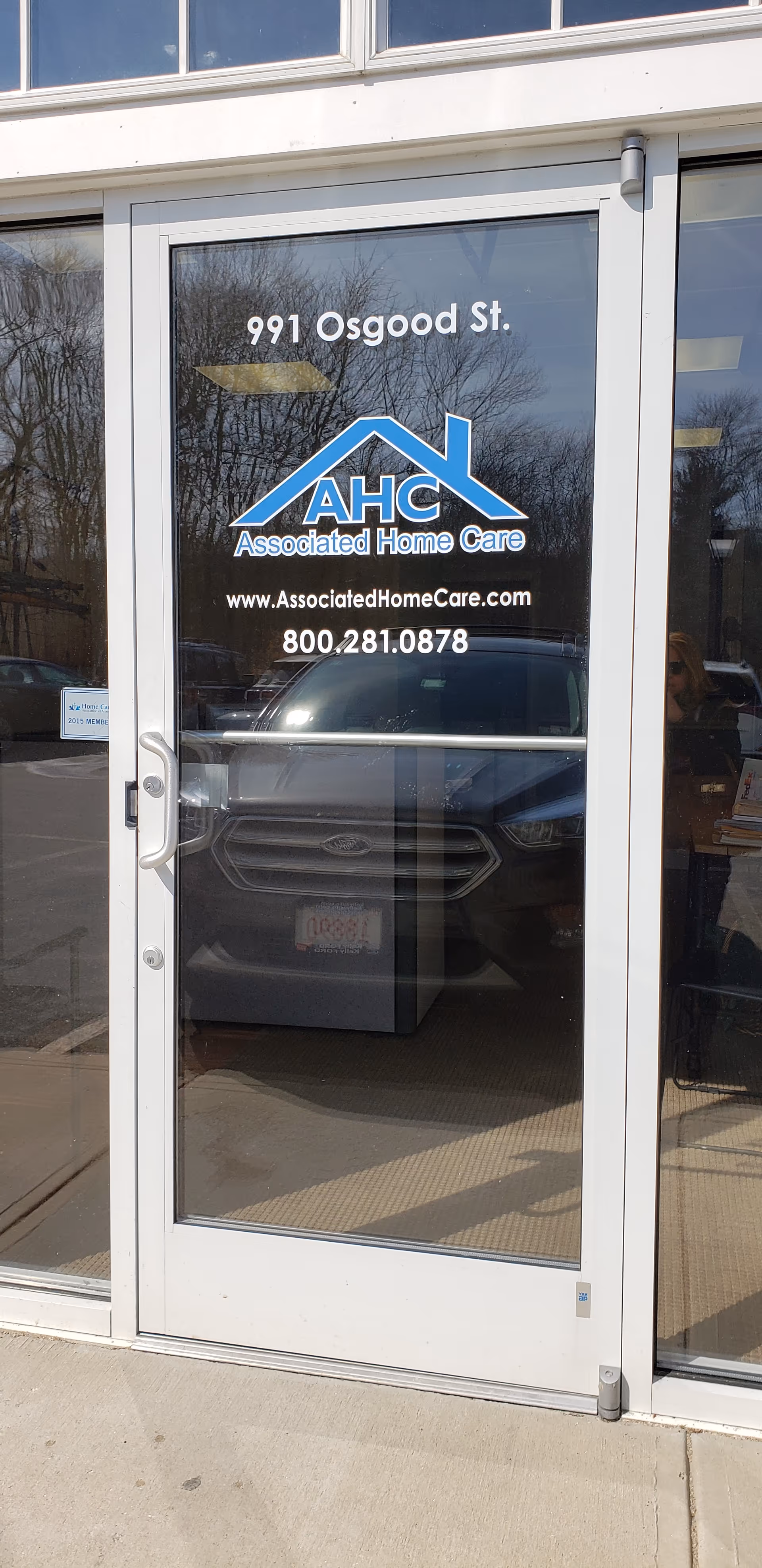 Glass storefront door with Associated Home Care logo and address reflected in the glass