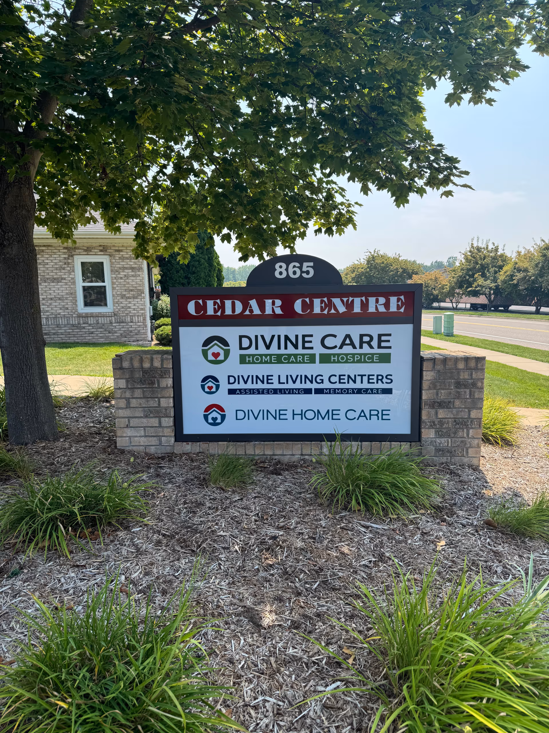 Exterior sign for Cedar Centre displaying Divine Care logos amid landscaped surroundings.