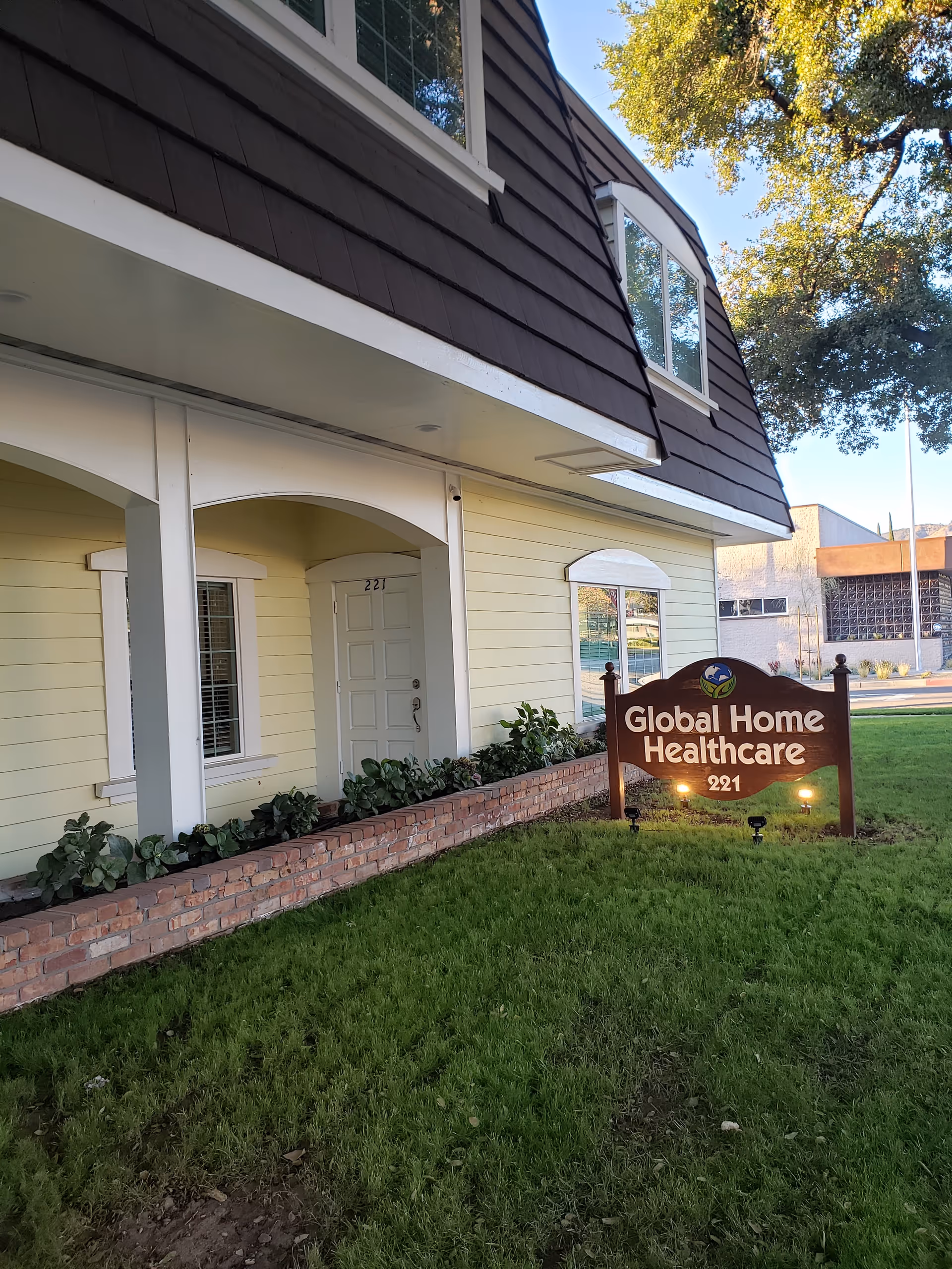 Exterior view of a light-yellow building with a Global Home Healthcare sign and greenery.