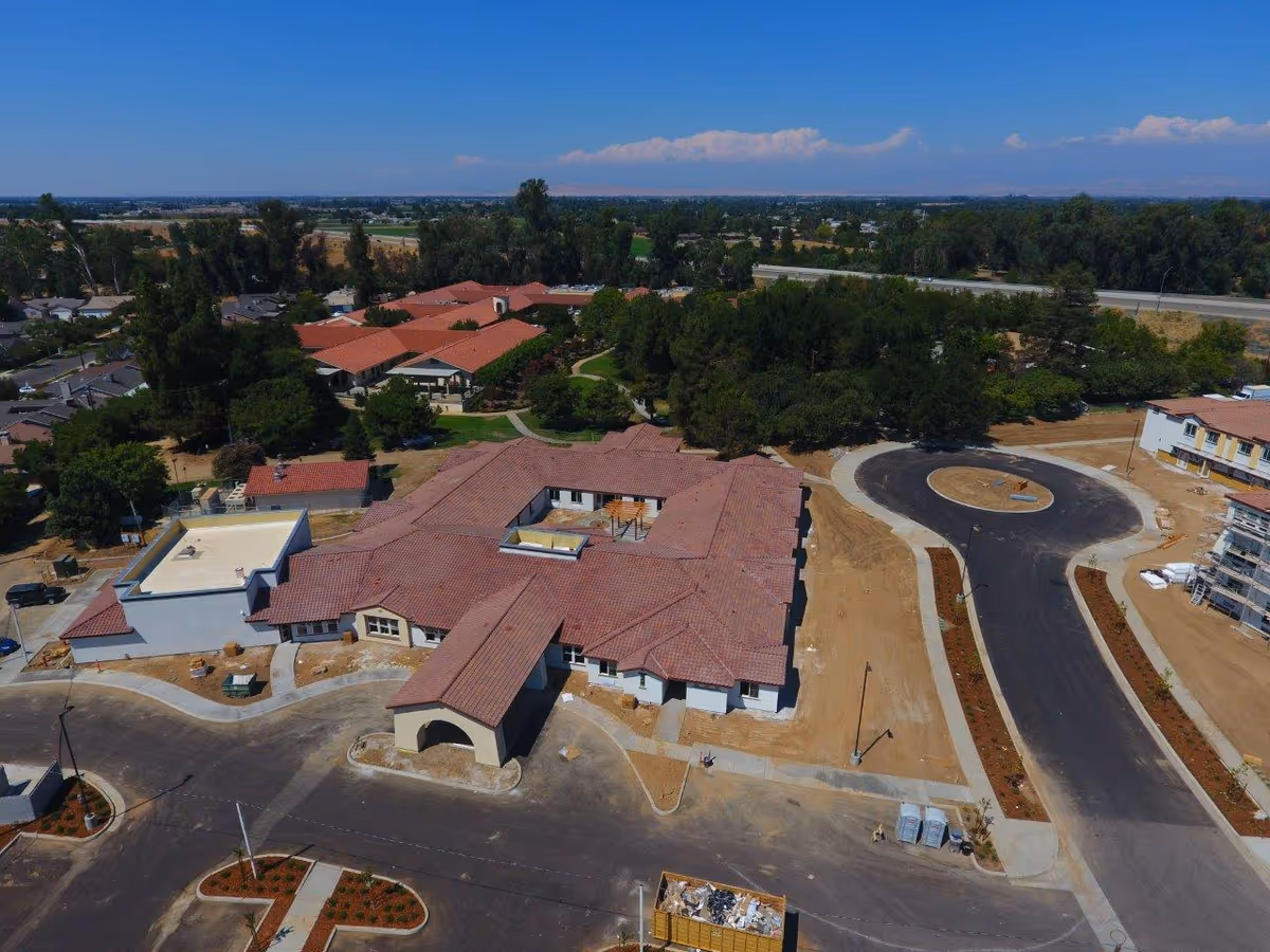 Aerial view of a senior living campus with red tiled roofs and surrounding roads.