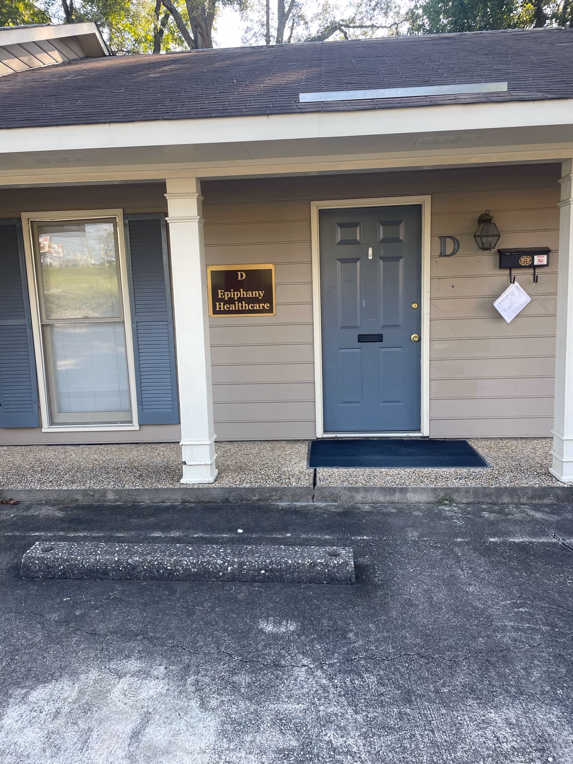Front exterior of Epiphany Healthcare facility featuring blue door, sign, porch columns, and parking.