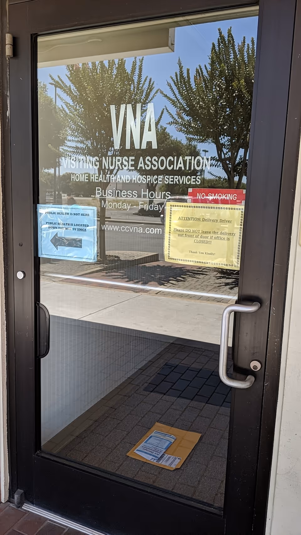 Glass entrance door with VNA signage and posted notices for Visiting Nurse Association.