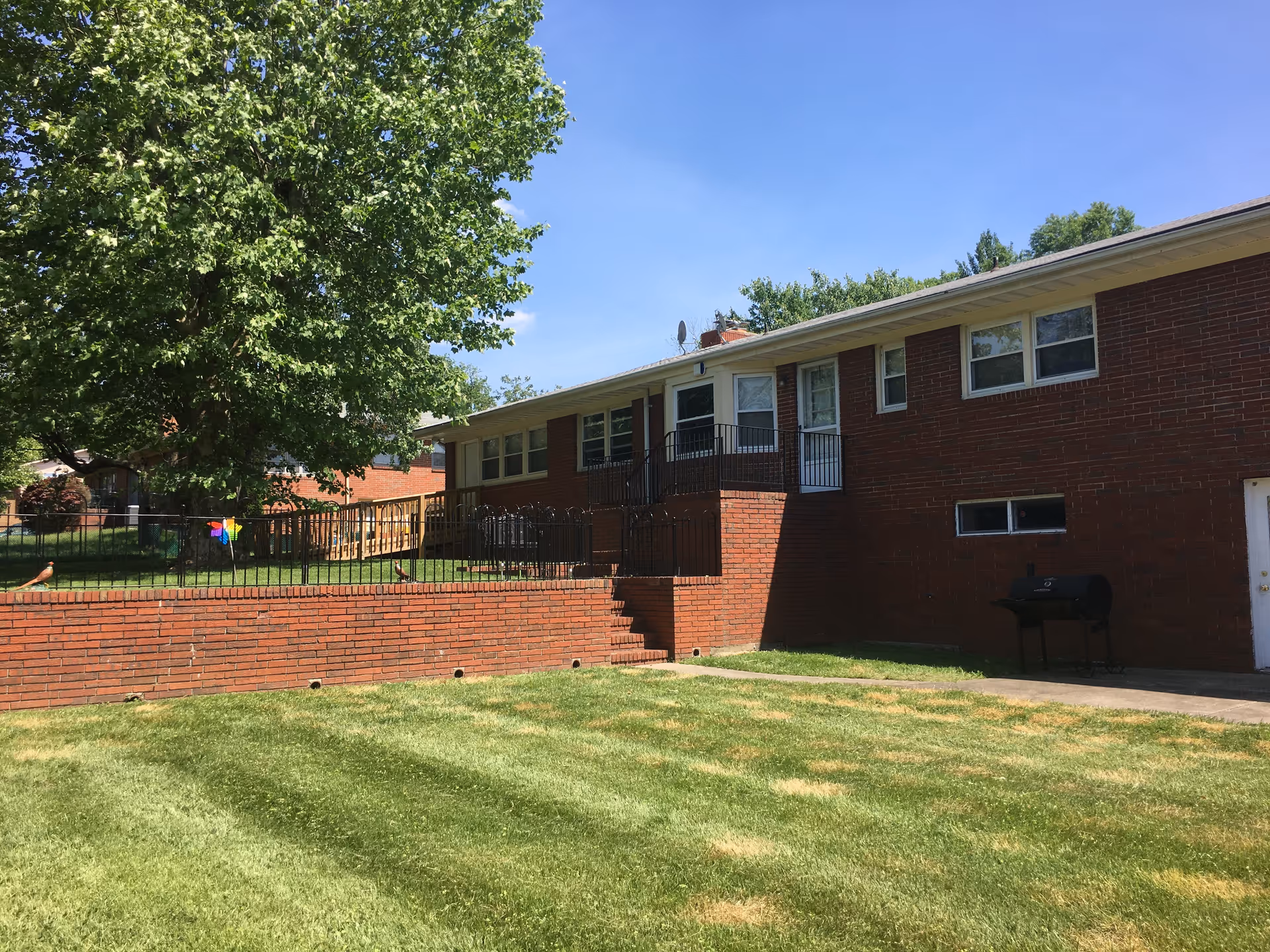 Brick senior living facility exterior with stairs, railing, and a large tree.