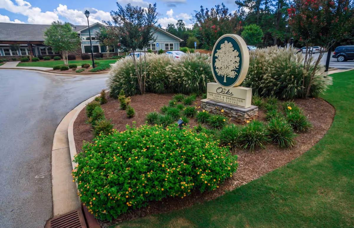 Entrance sign for Oaks at Braselton, surrounded by landscaped shrubs and a curved driveway.