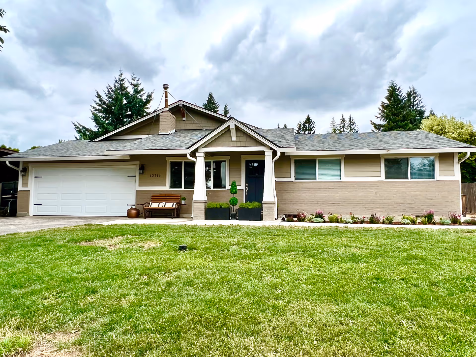 Front view of a single-story home with a porch, two-car garage, and well-kept lawn.