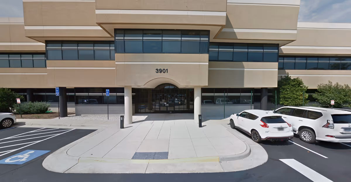 Exterior view of a senior living facility entrance with curved sidewalk and parking.