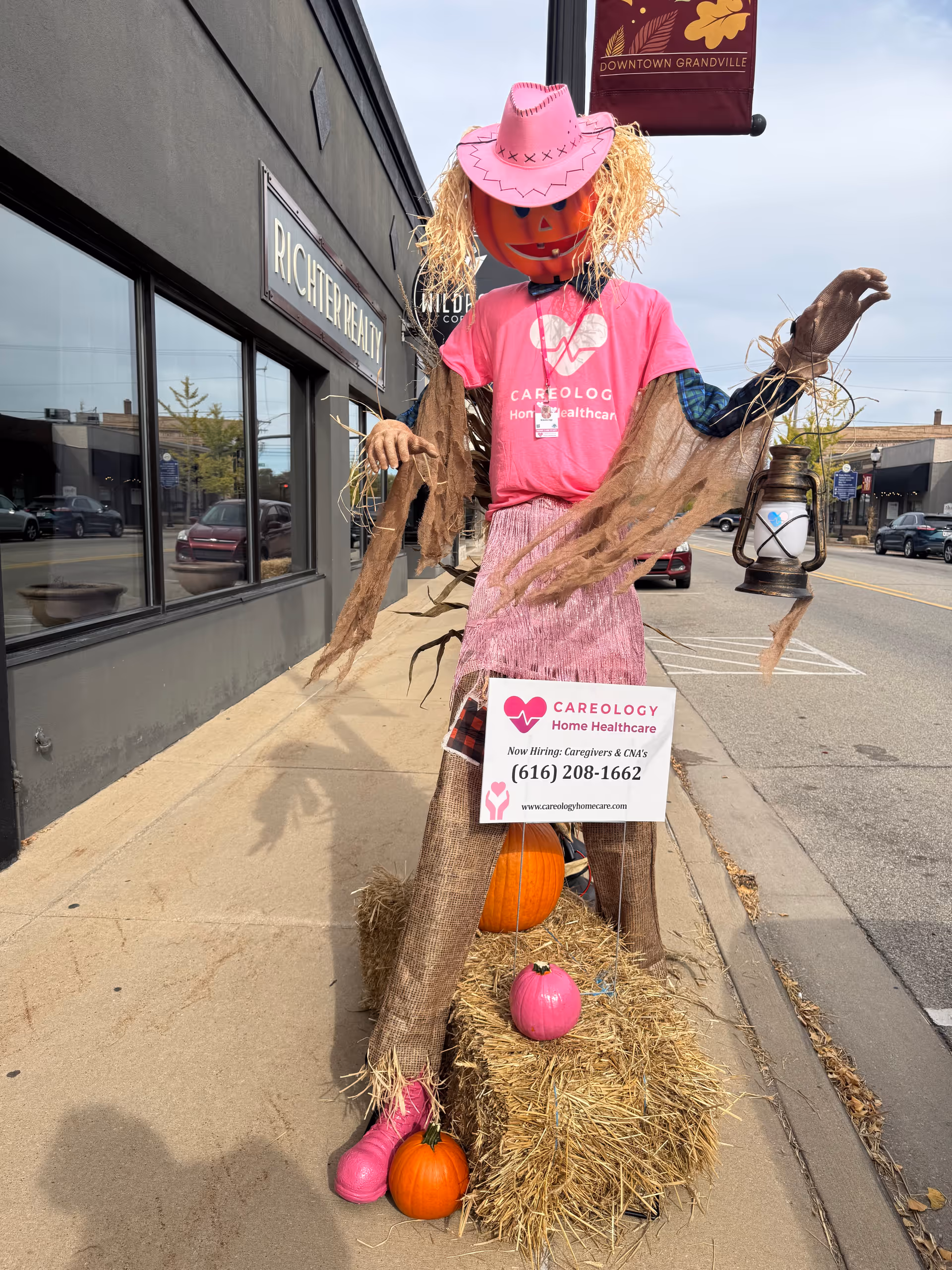 Seasonal scarecrow display in front of Careology Home Healthcare storefront on a sidewalk.