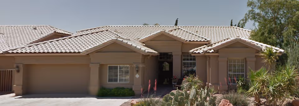 Single-story tan building with a tile roof and desert landscaping at the entrance.