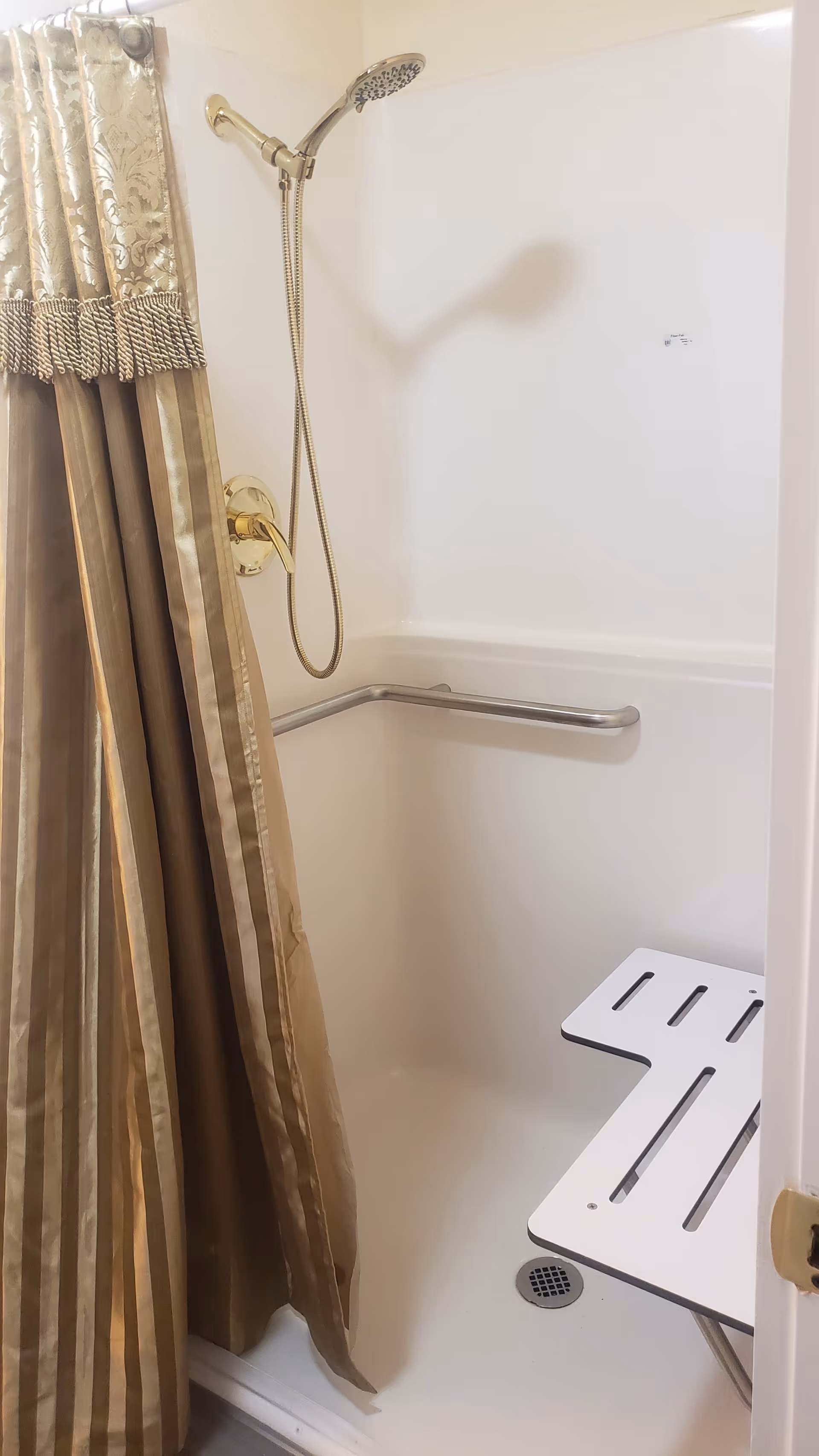Accessible bathroom shower with handheld showerhead, grab bar, and fold-down seat.