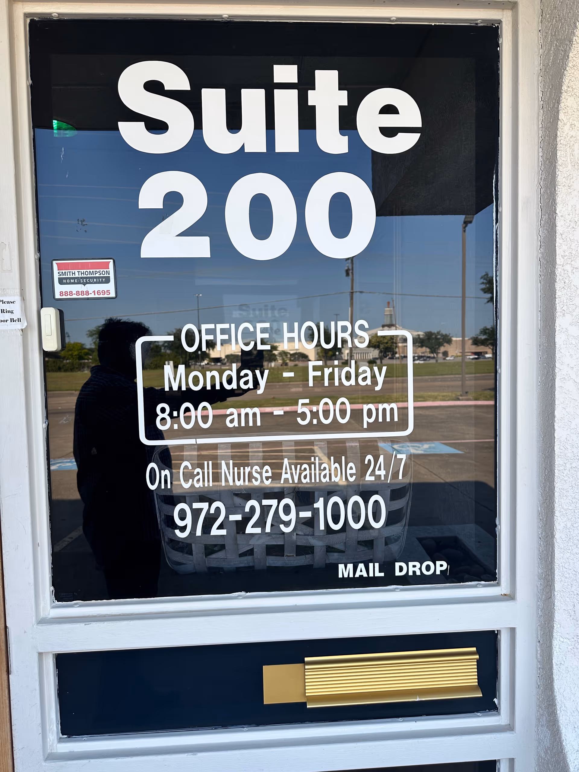Front glass door displays Suite 200 and office hours with parking lot reflection