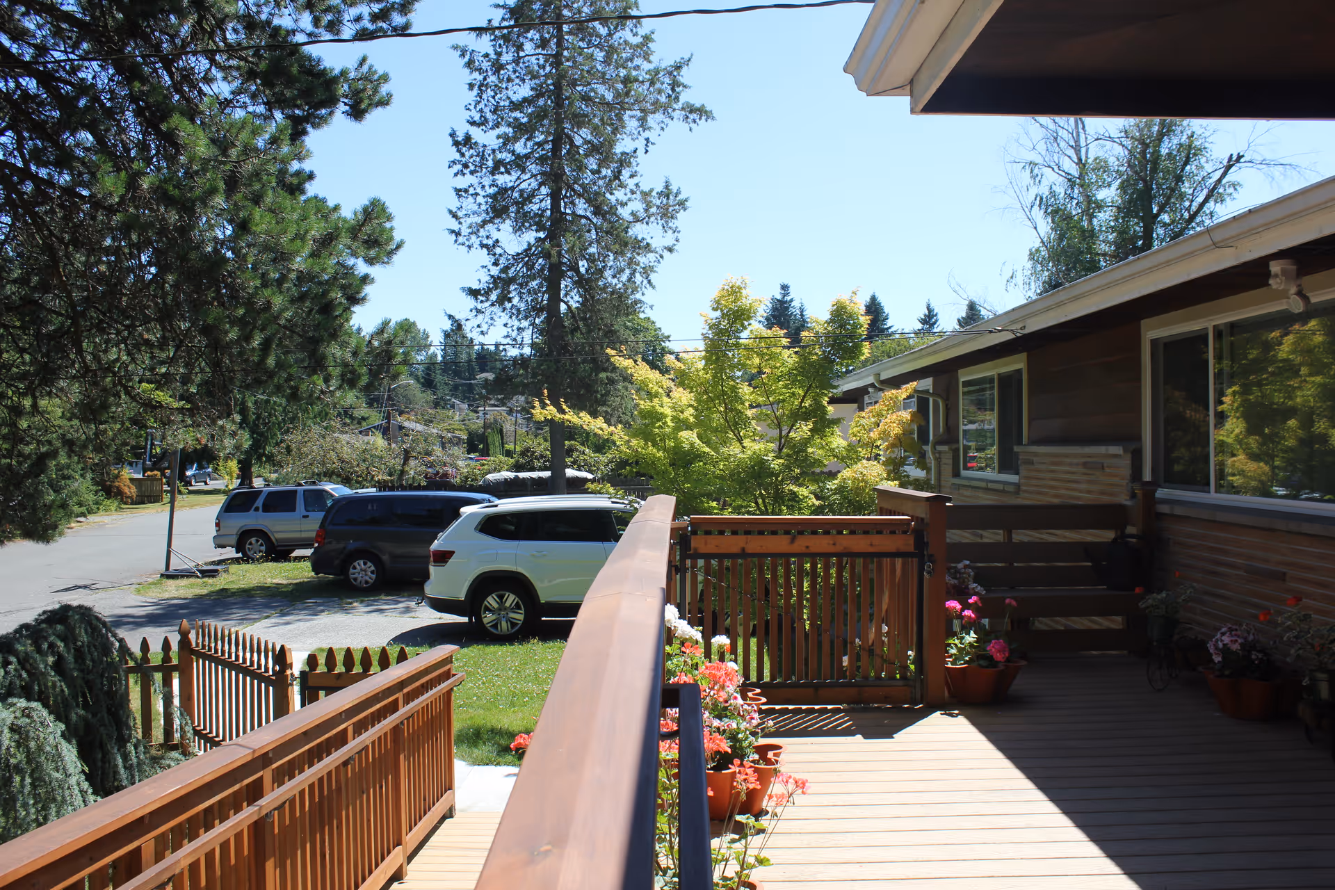 Wooden deck and railing of a senior living home with potted plants and parked cars.