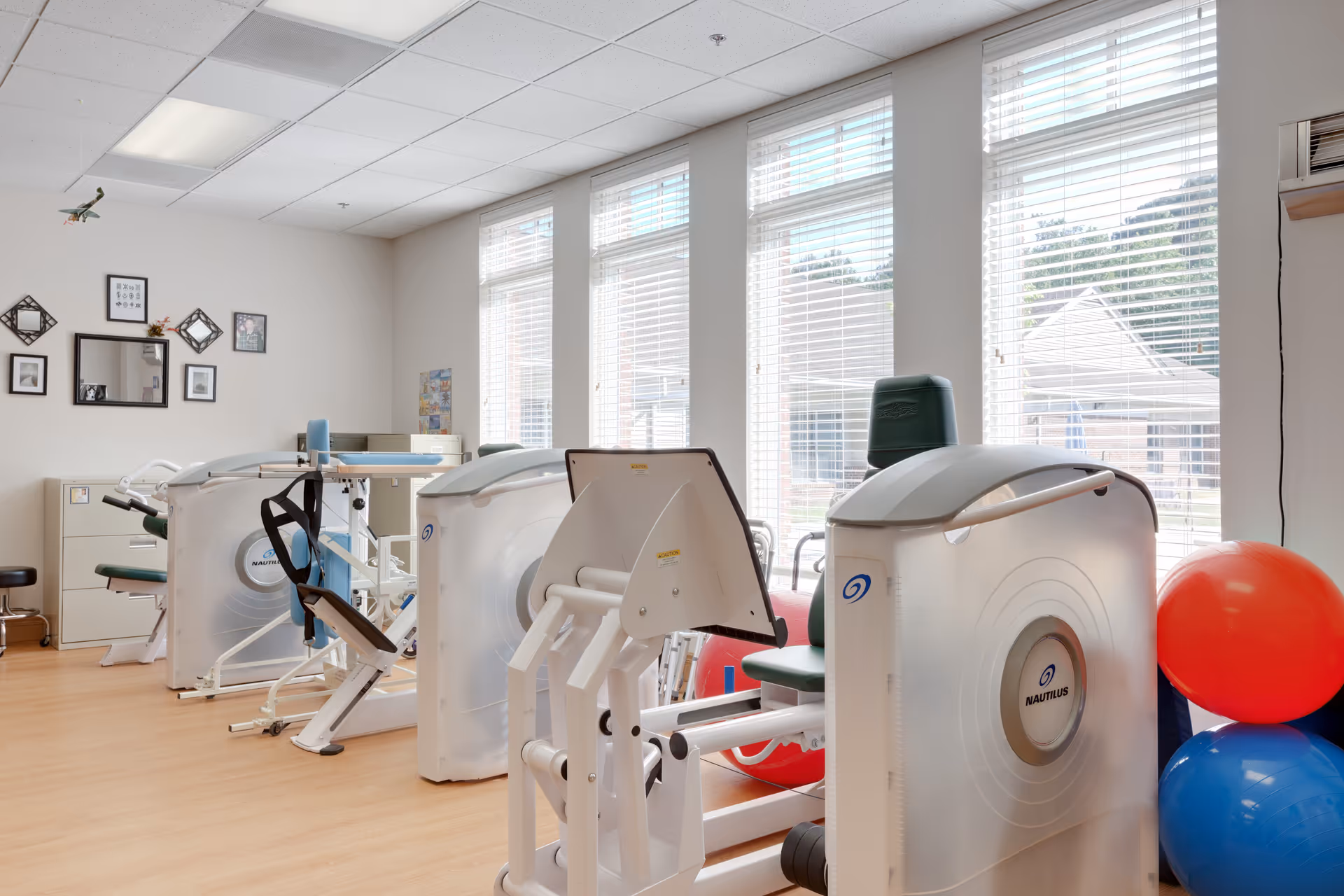 Bright indoor fitness room with Nautilus machines, balls, and large windows.
