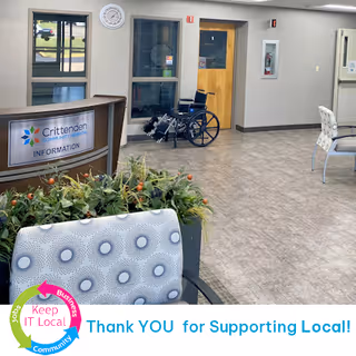 Lobby area with information desk, wheelchair, chairs, and potted plants in a hospital corridor.