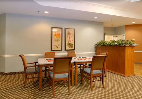 Senior living dining area with round table, six chairs, and a plant-filled counter.