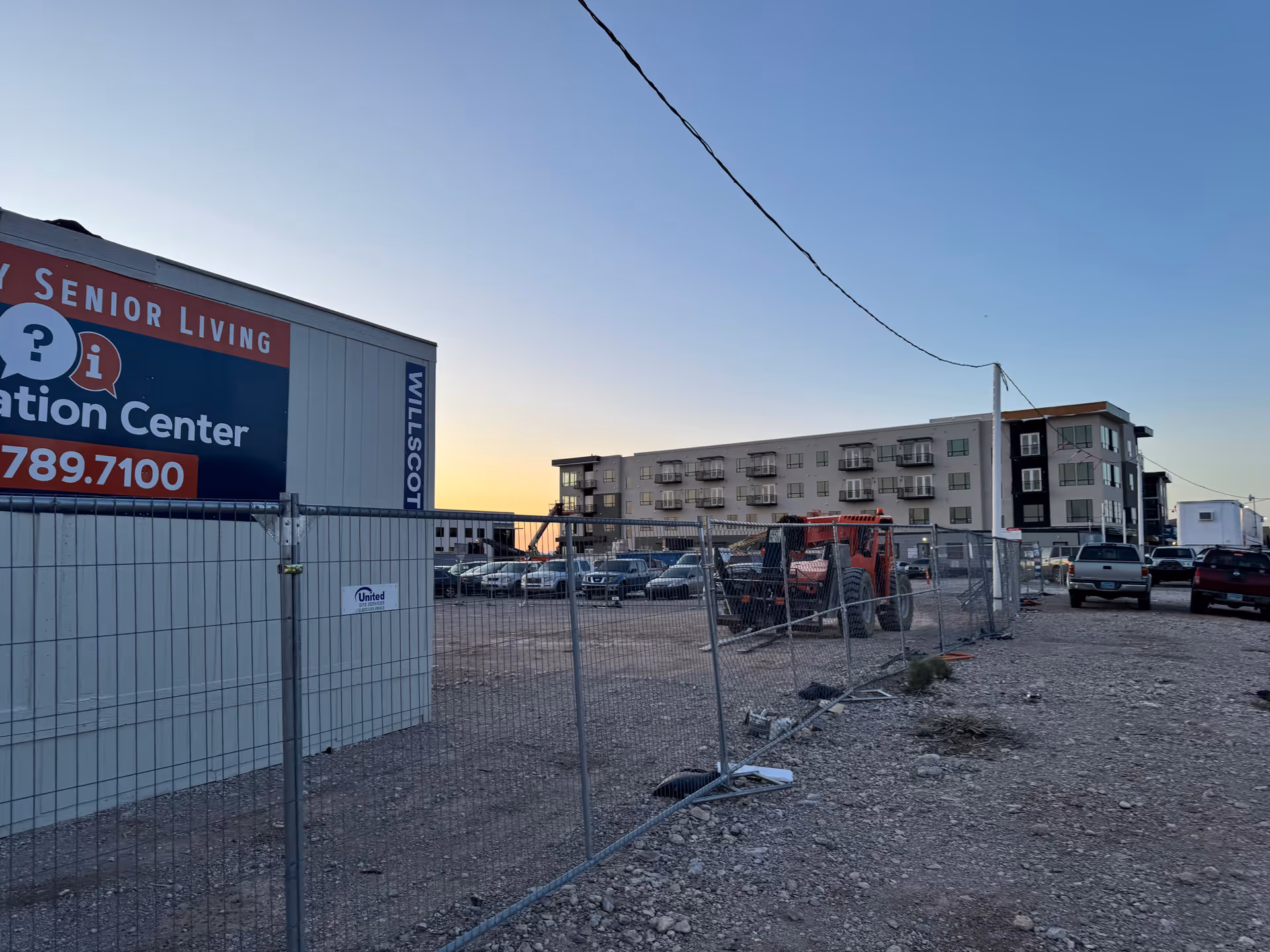 Exterior view of a construction site with a building and chain-link fence at sunset.