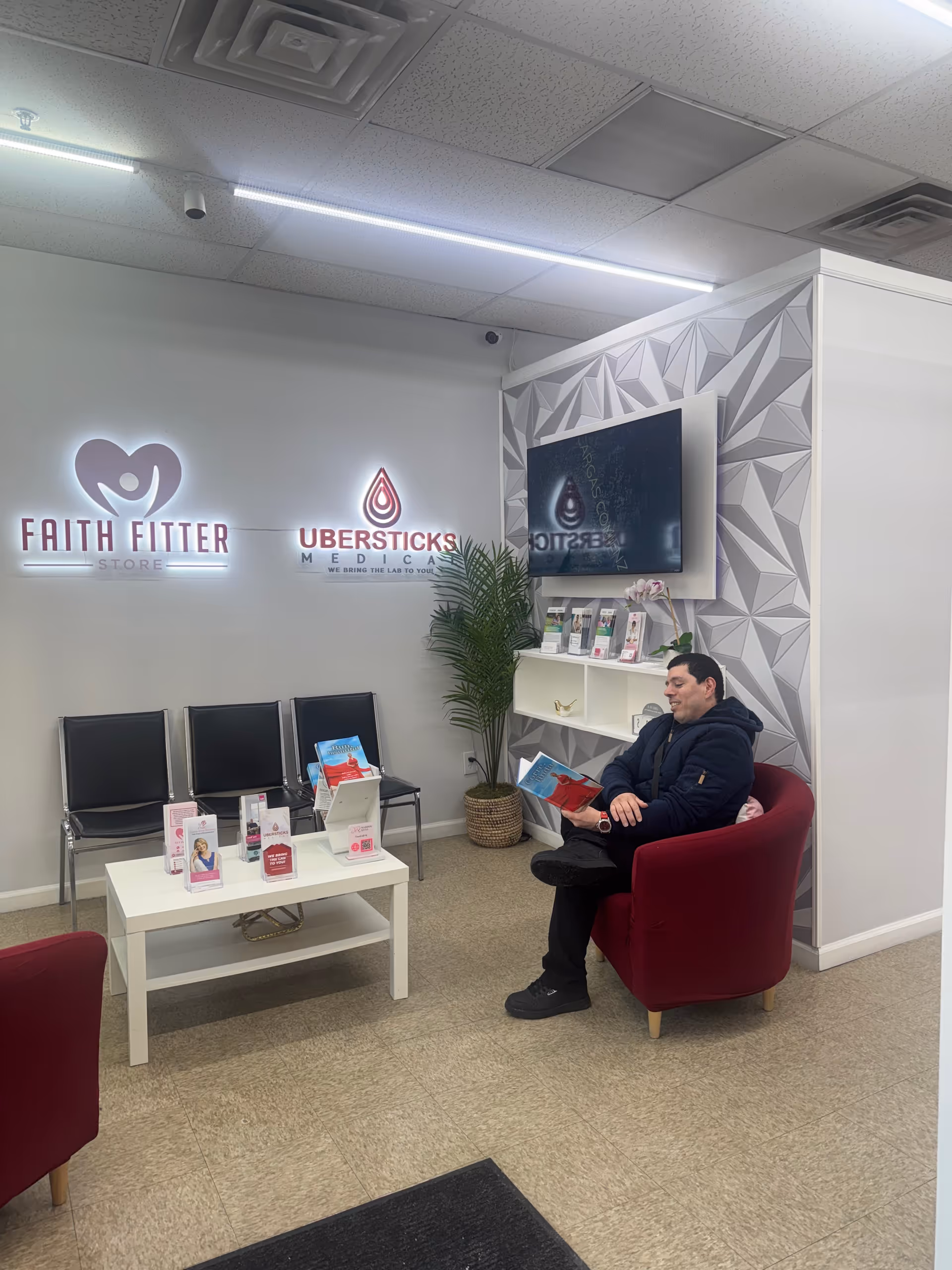 A man sits in a red armchair reading brochures in a modern clinic reception area.