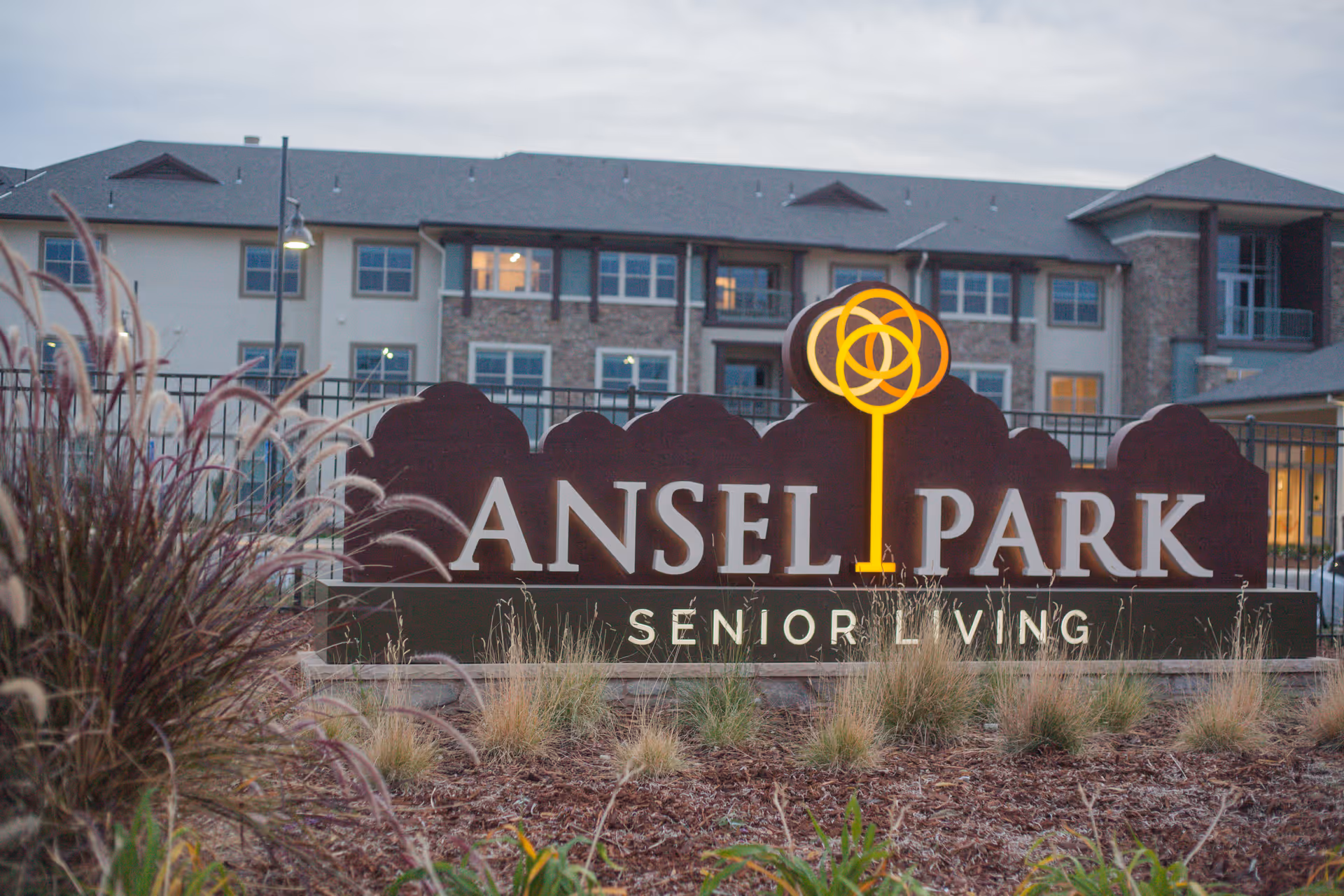 A large sign reading "Ansel Park Senior Living" stands in landscaped grounds with the facility building behind it.