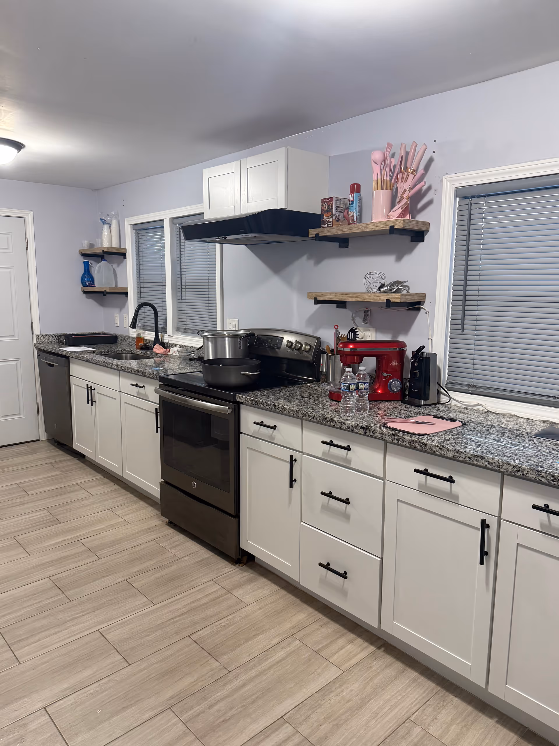 Long kitchen with white cabinets, granite counters, stove, sink, and shelves in a senior living facility.