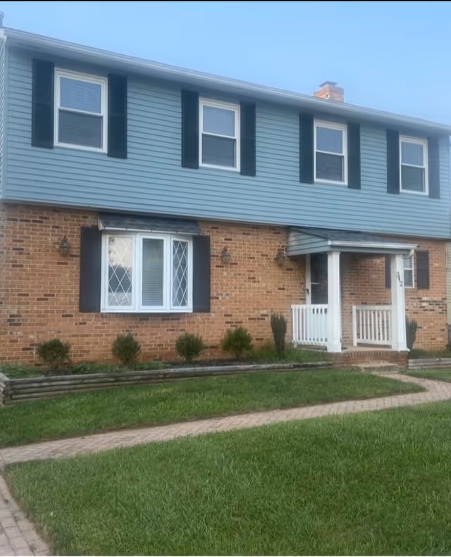 Two-story brick and blue siding building with white porch and black shutters.